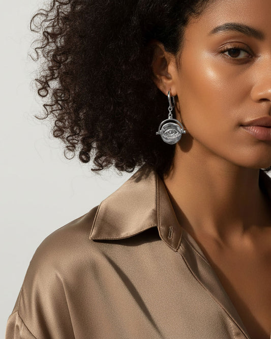 Model wearing a pair of silver hoop earrings featuring an evil eye round charm.