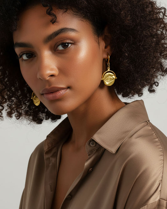 Model wearing a pair of gold hoop earrings featuring an evil eye round charm.