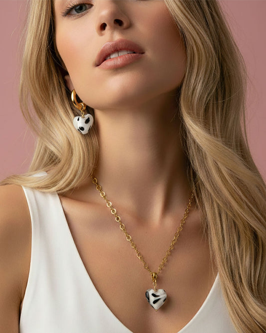 Woman wearing the Heart Bundle set gold hoop earrings with black and white heart charm and matching necklace