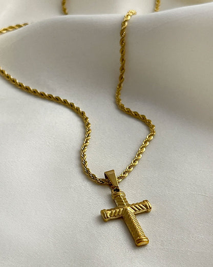 A gold rope chain necklace with a gold cross pendant. The cross has a textured design.