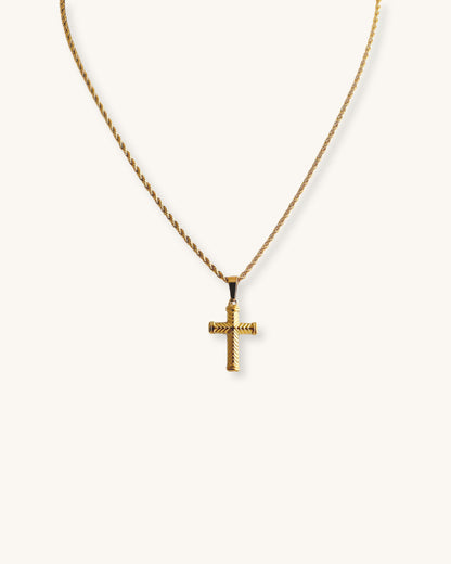 A gold rope chain necklace with a gold cross pendant. The cross has a textured design.