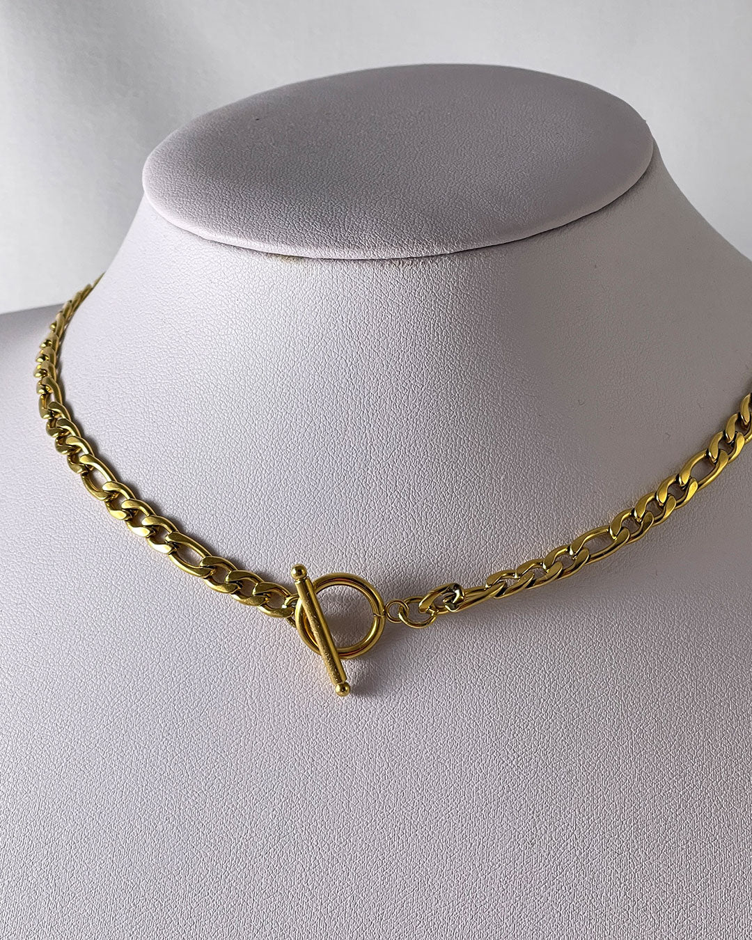 A figaro chain necklace in gold with a toggle clasp closure