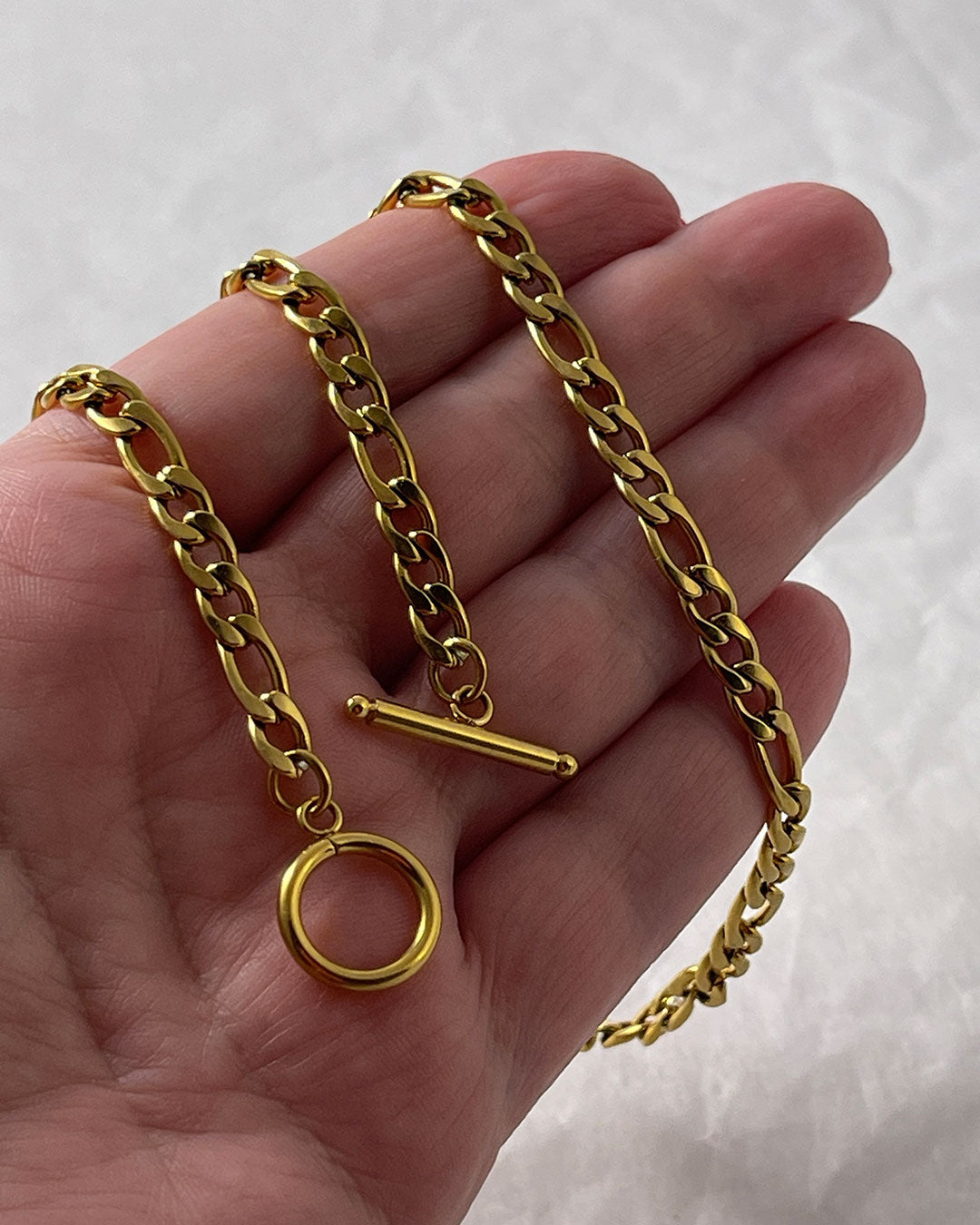 A figaro chain necklace in gold with a toggle clasp closure