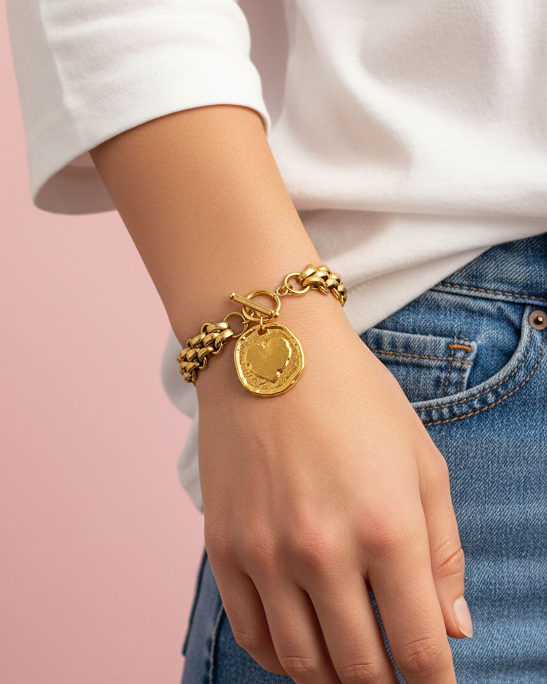 Gold multilink chain bracelet with a heart coin charm on the wrist 