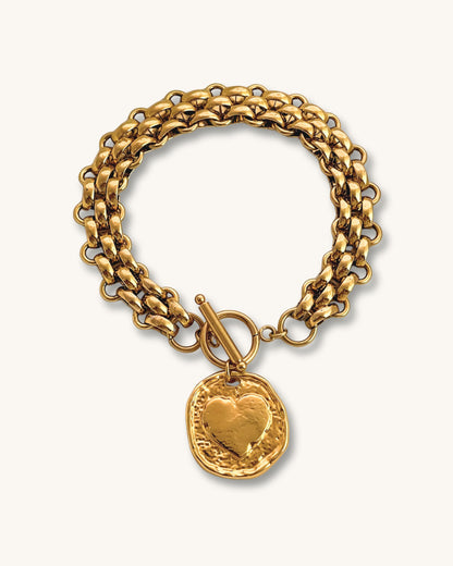 Gold multilink chain bracelet with a heart coin charm on a white background