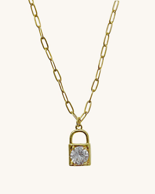 A gold chain necklace with a padlock pendant. The padlock has a clear crystal in the center.