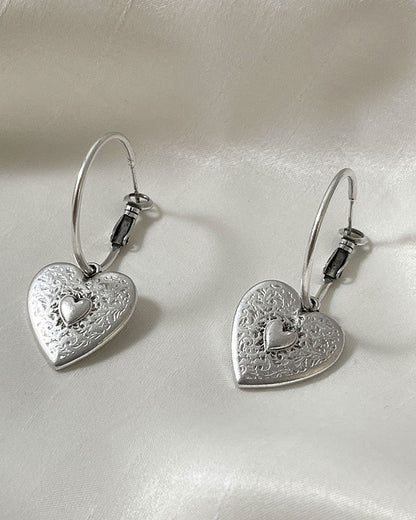 The Heart Hoop Earrings, a pair of silver hoop earrings featuring a heart charm.