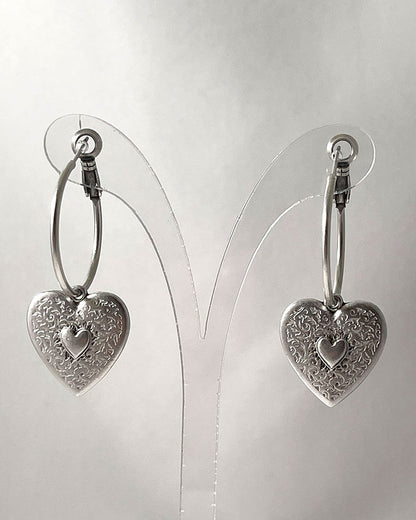 The Heart Hoop Earrings, a pair of silver hoop earrings featuring a heart charm.