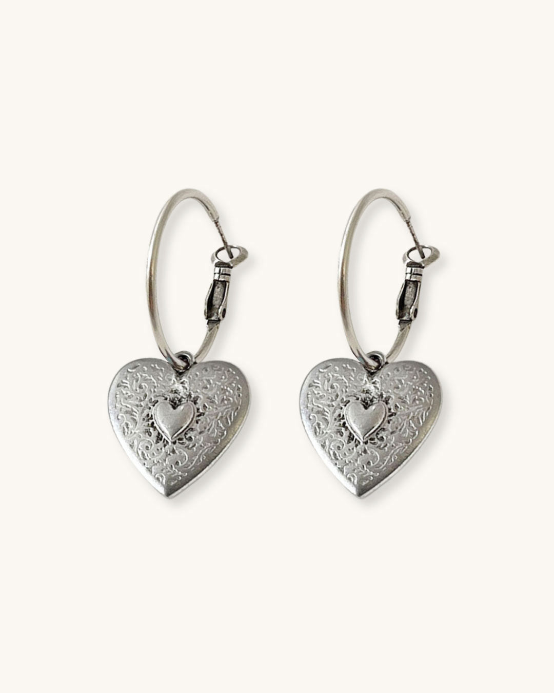 The Heart Hoop Earrings, a pair of silver hoop earrings featuring a heart charm.