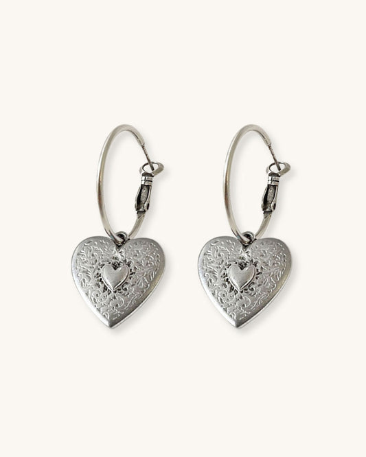 The Heart Hoop Earrings, a pair of silver hoop earrings featuring a heart charm.