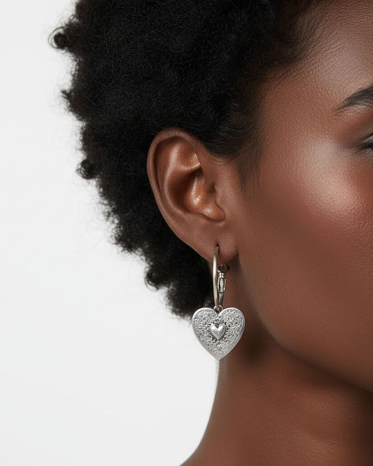Woman wearing a pair of silver hoop earrings with heart charms