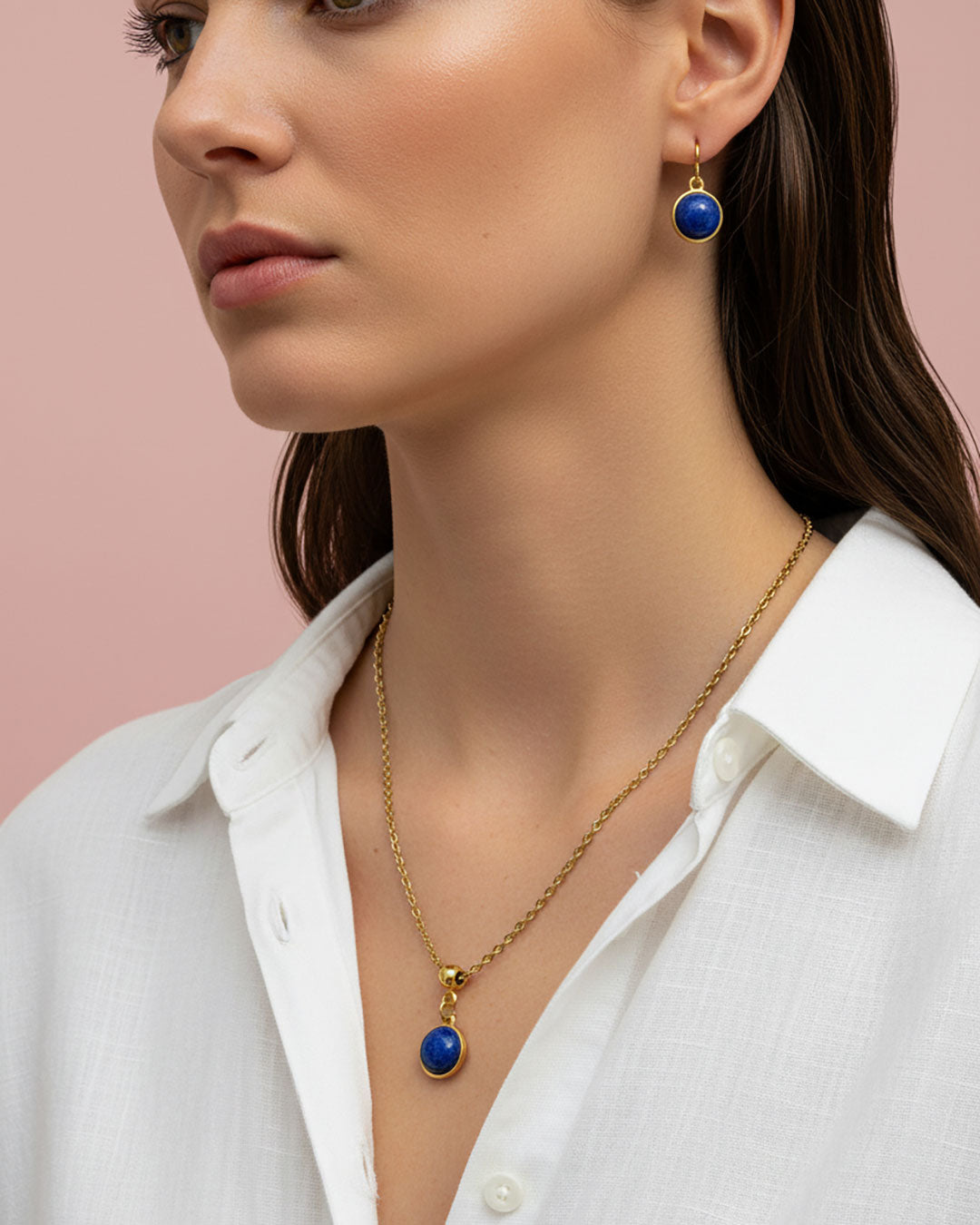 Woman wearing a gold necklace with a lapis lazuli pendant against a pink background