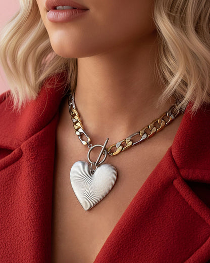 Model wearing a two tone chunky figaro chain necklave with a large heart pendant in silver.