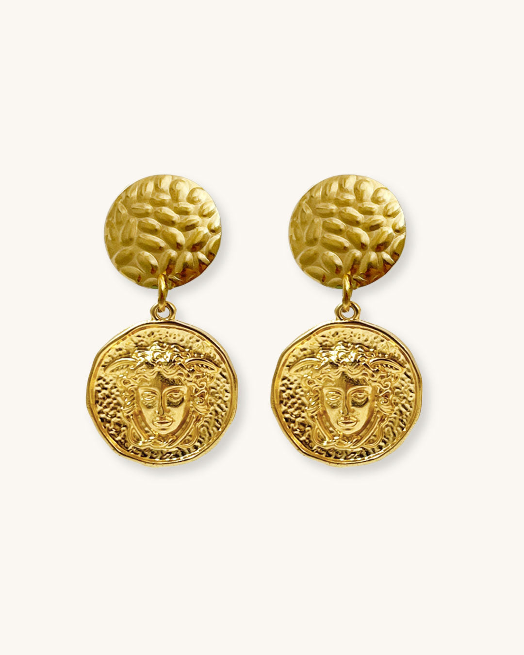 The Medusa Earrings, a pair of gold earrings featuring a round medusa head charm.