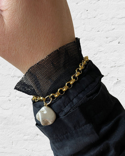 Gold chain bracelet with a MOP shell pearl charm on a wrist against a white background
