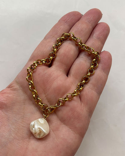 Gold chain bracelet with a MOP shell pearl pendant on a hand against a white background