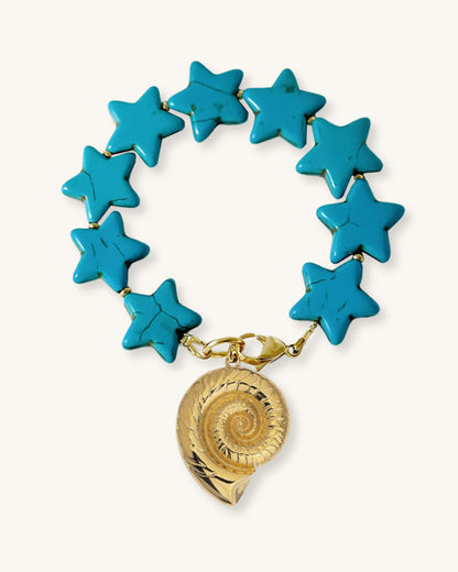 Bracelet with turquoise star-shaped howlite beads and a large gold nautilus shell charm on a white fabric background