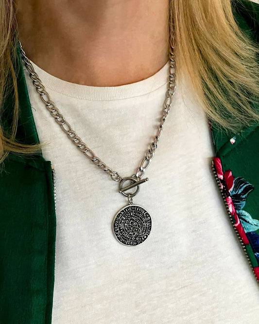 Model wearing figaro chain necklace in silver featuring a Phaistos disc pendant and a toggle closure.