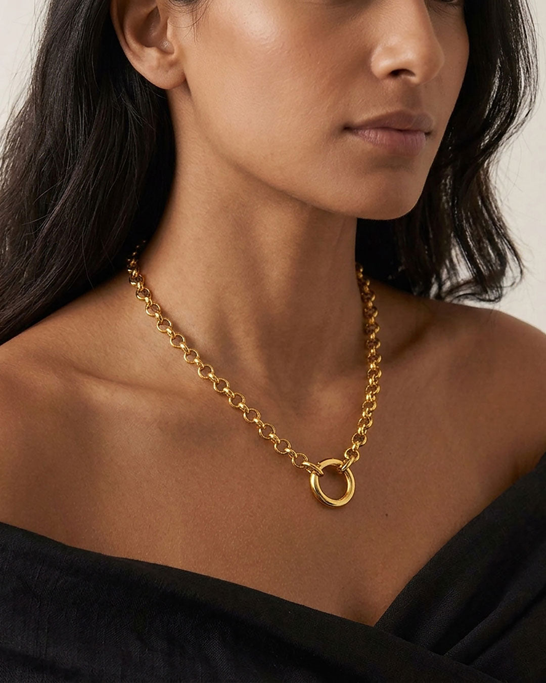 A close up of a woman's neck wearing a gold rolo chain necklace with a simple circular closure