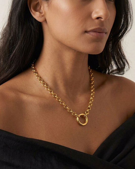 A close up of a woman's neck wearing a gold rolo chain necklace with a simple circular closure