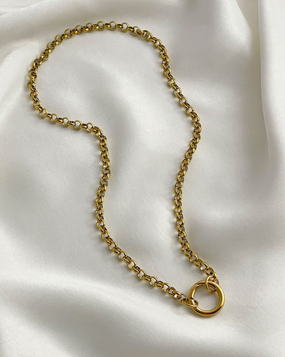 A close up of a gold rolo chain necklace with a simple circular closure on a white fabric