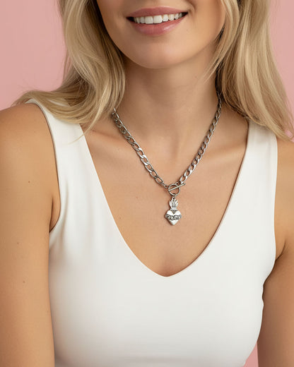 Woman wearing a silver chain necklace with a heart pendant against a pink background