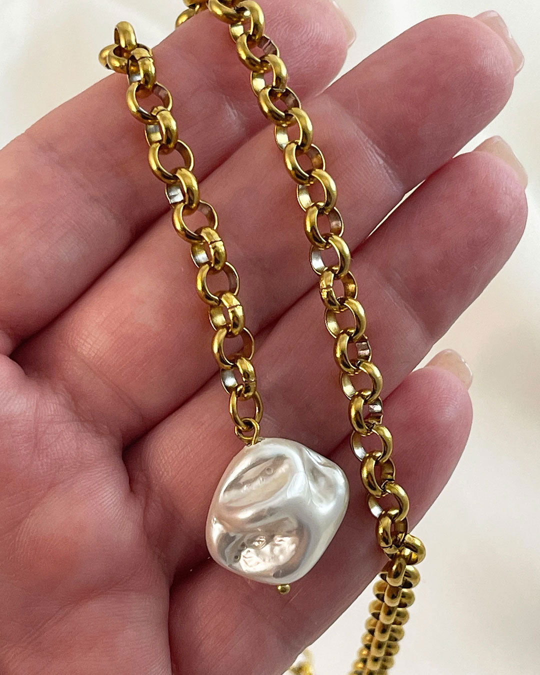 Gold chain necklace with a large MOP pearl pendant held in a hand against a neutral background