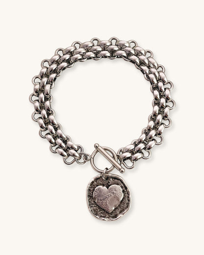 Silver multilink chain bracelet with a heart coin charm on a white background