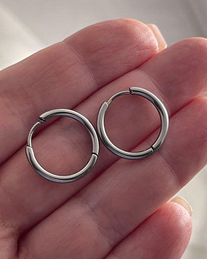 Pair of silver hoop earrings 14mm held between fingers against a neutral background