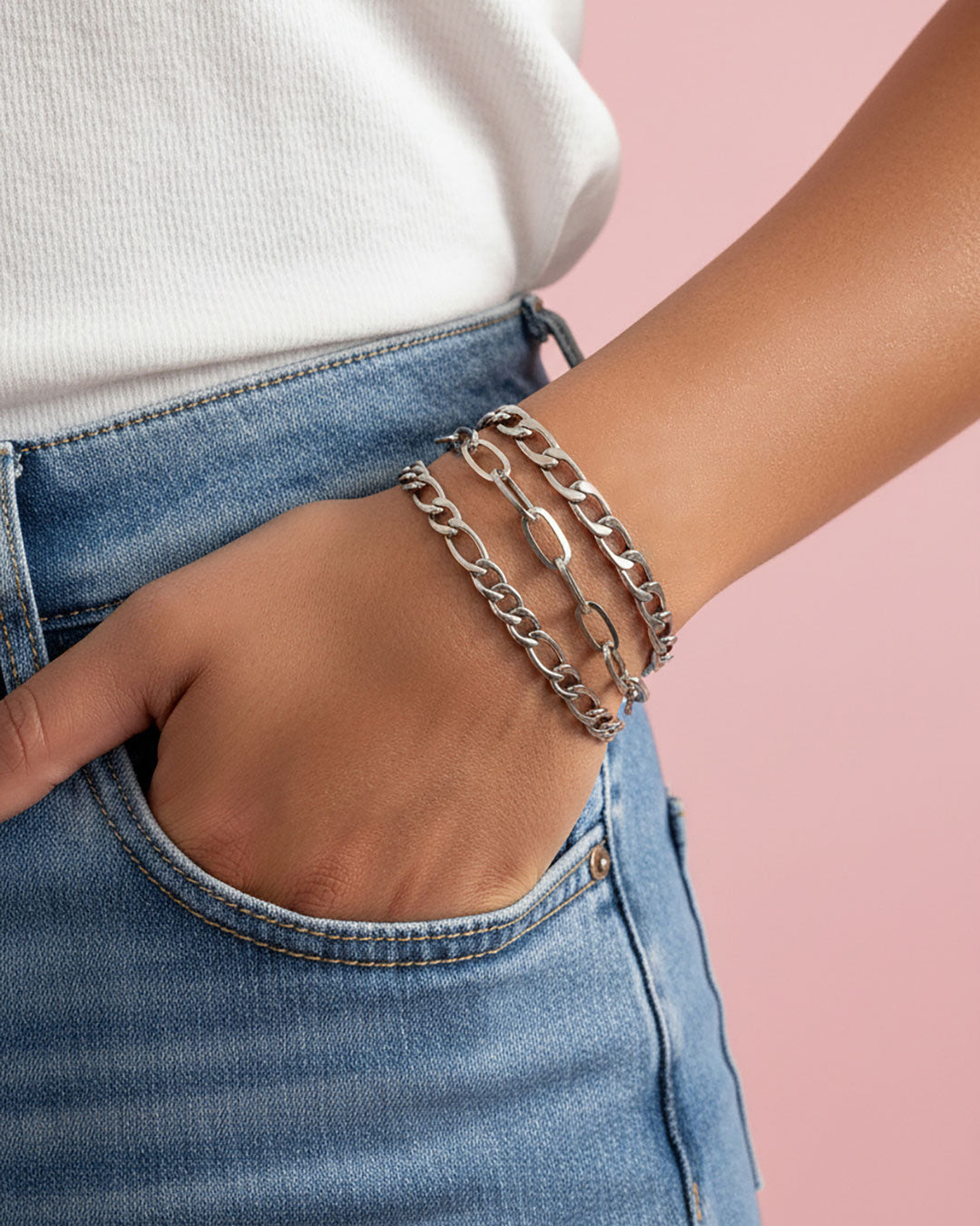 Model wearing three silver chain bracelets with different link styles. The bracelets are all different widths and have a curb chain, paperclip and a figaro chain design.
