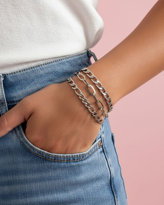 Model wearing three silver chain bracelets with different link styles. The bracelets are all different widths and have a curb chain, paperclip and a figaro chain design.