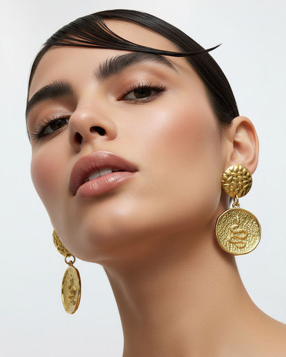 Model wearing a pair of gold earrings featuring a round snake charm.