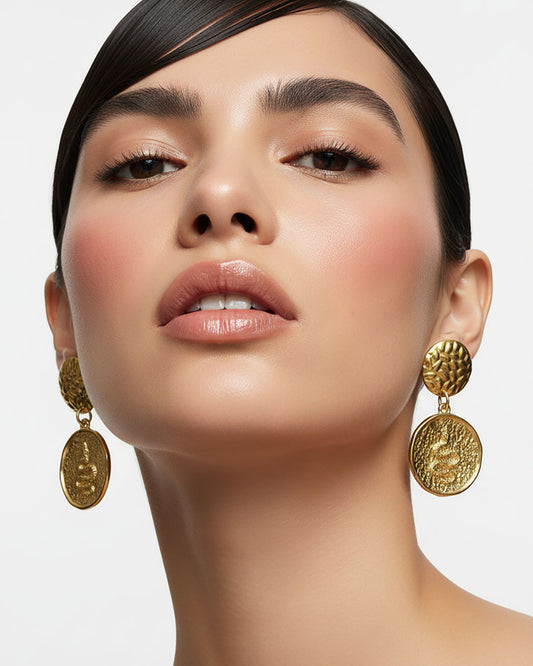 Model wearing a pair of gold earrings featuring a round snake charm.