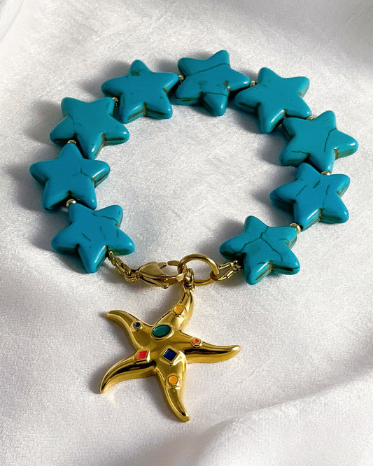 Turquoise star-shaped howlite beaded bracelet with a gold starfish charm on a white background