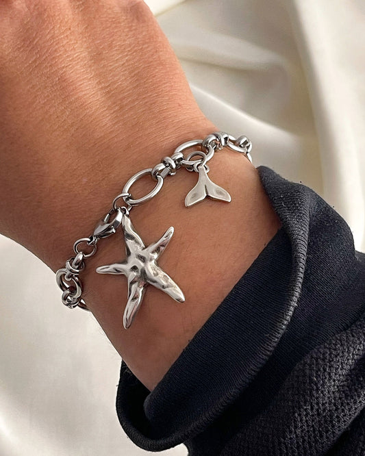 Silver chain bracelet with starfish charm on a wrist against a neutral background