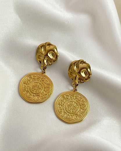 Pair of gold drop earrings with an ethnic design coin charm on a white background