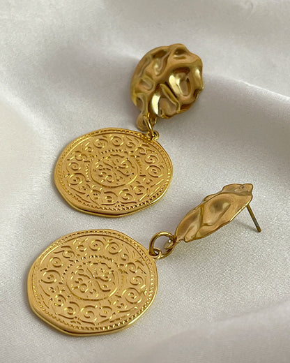 Pair of gold drop earrings with an ethnic design coin charm on a white background