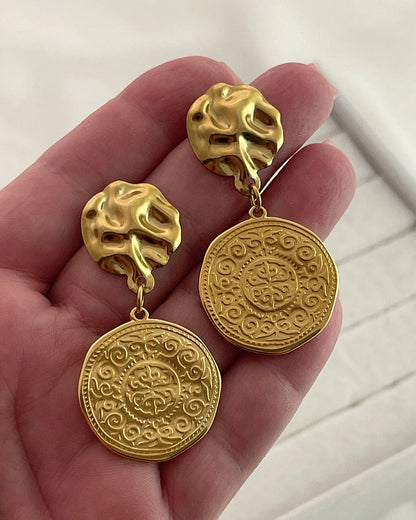 Pair of gold drop earrings with an ethnic design coin charm on a white background