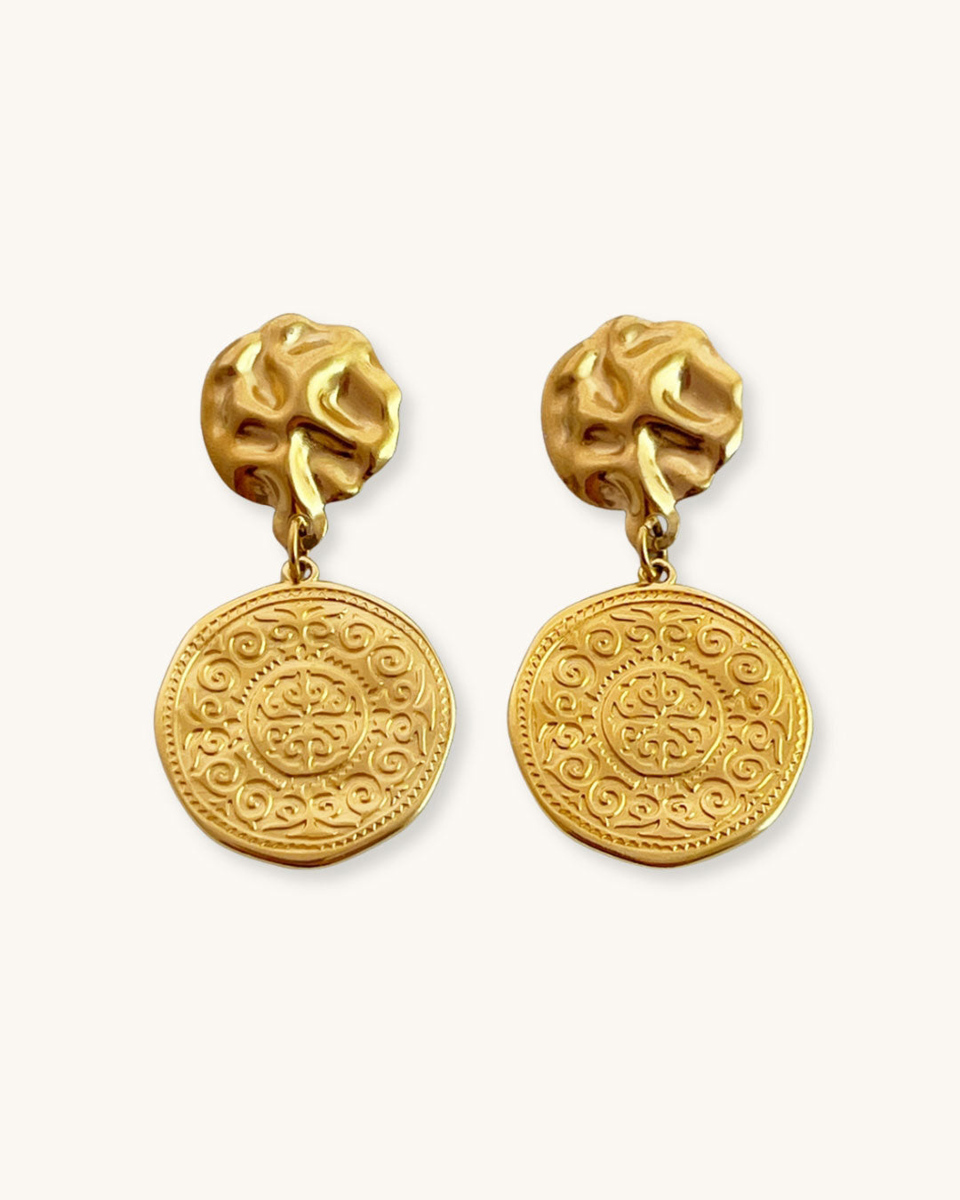 Pair of gold drop earrings with an ethnic design coin charm on a white background