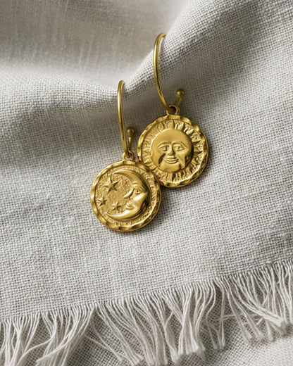 A pair of gold open hoop earrings featuring a round double faced sun moon charm.