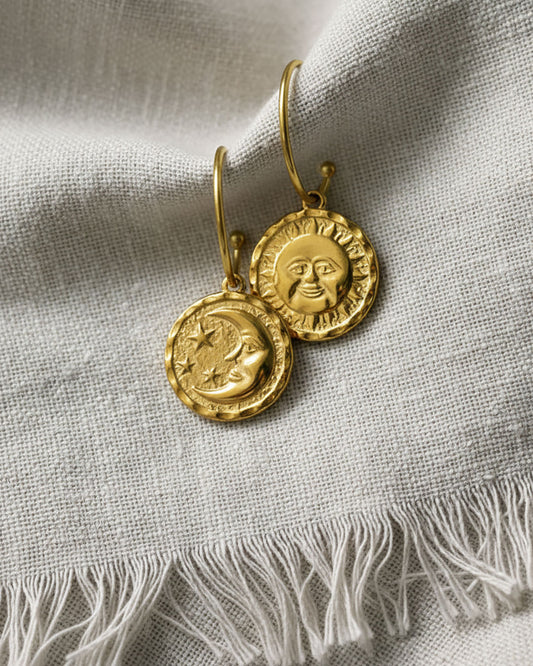 A pair of gold open hoop earrings featuring a round double faced sun moon charm.