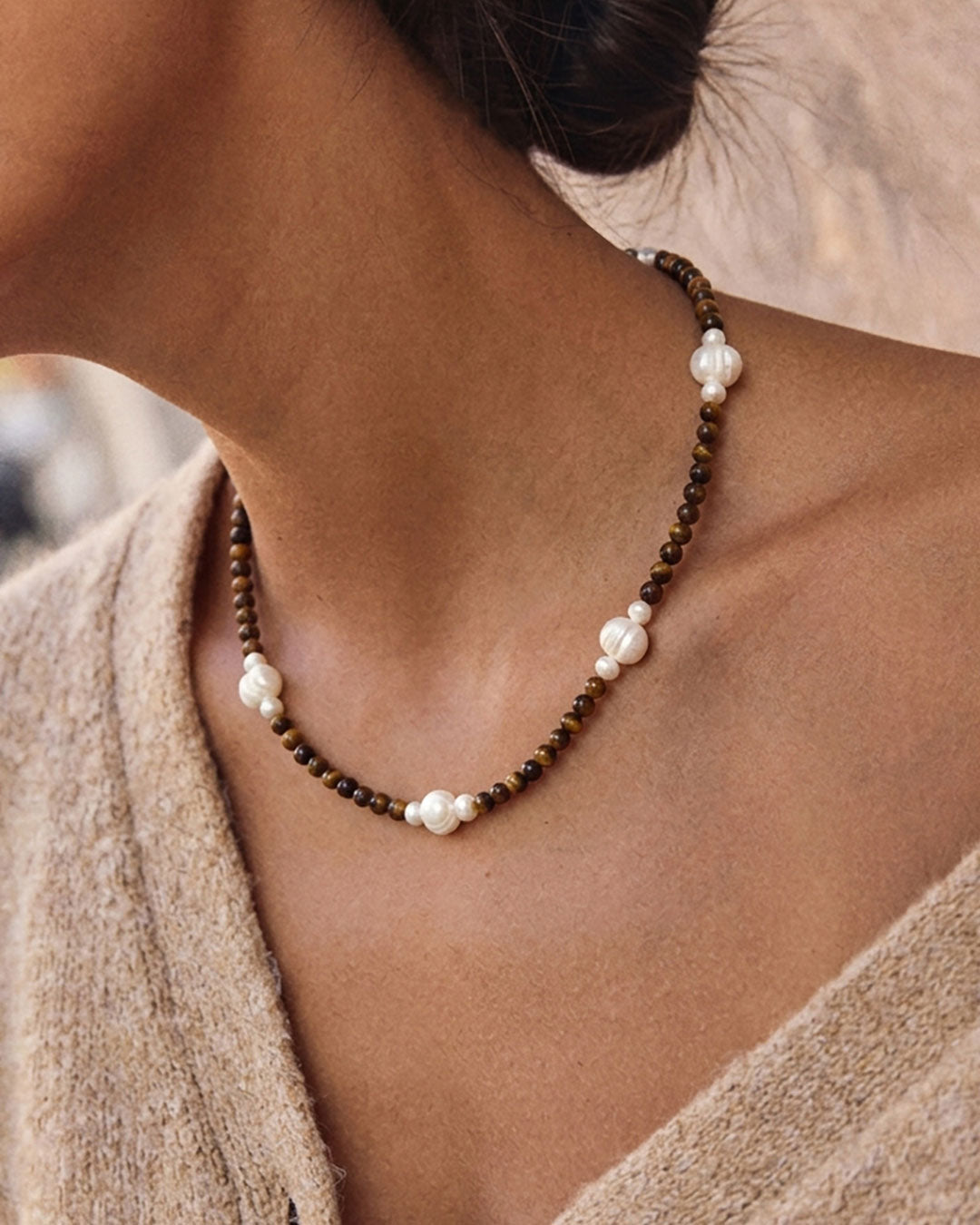 A gold chain necklace with brown tiger eye beads and white pearl accents on a woman’s neck 