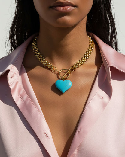 Model wearing a chunky gold chain necklace with a turquoise heart pendant