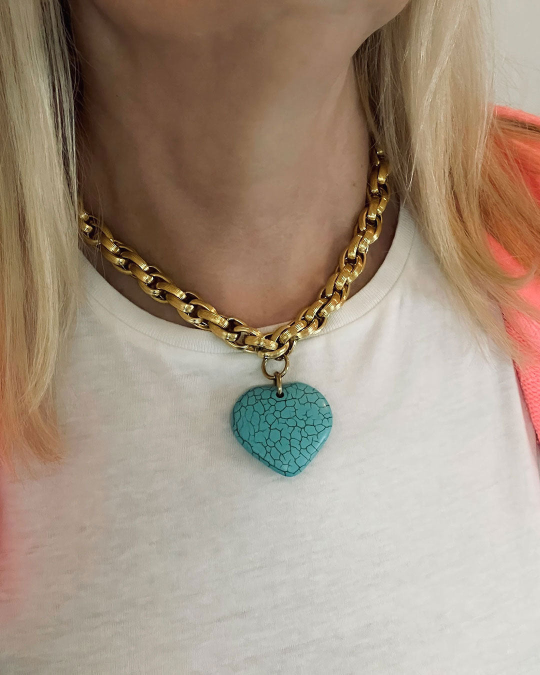 Gold chain necklace with a turquoise heart pendant worn by a person.