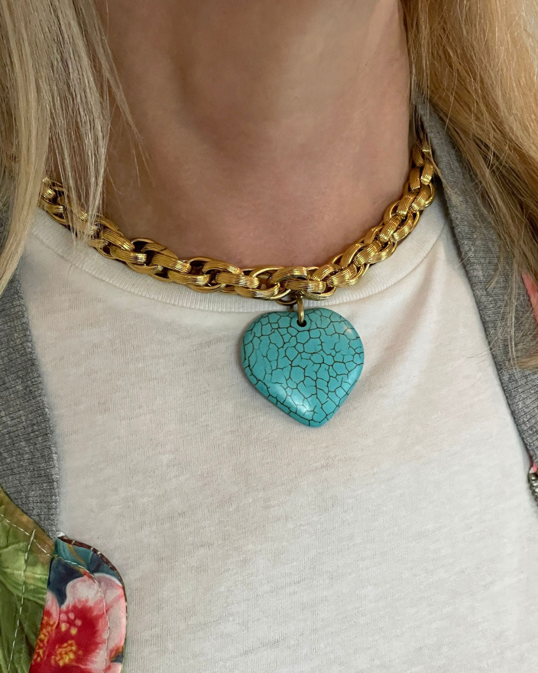 Model wearing a gold chain necklace with a turquoise heart pendant 