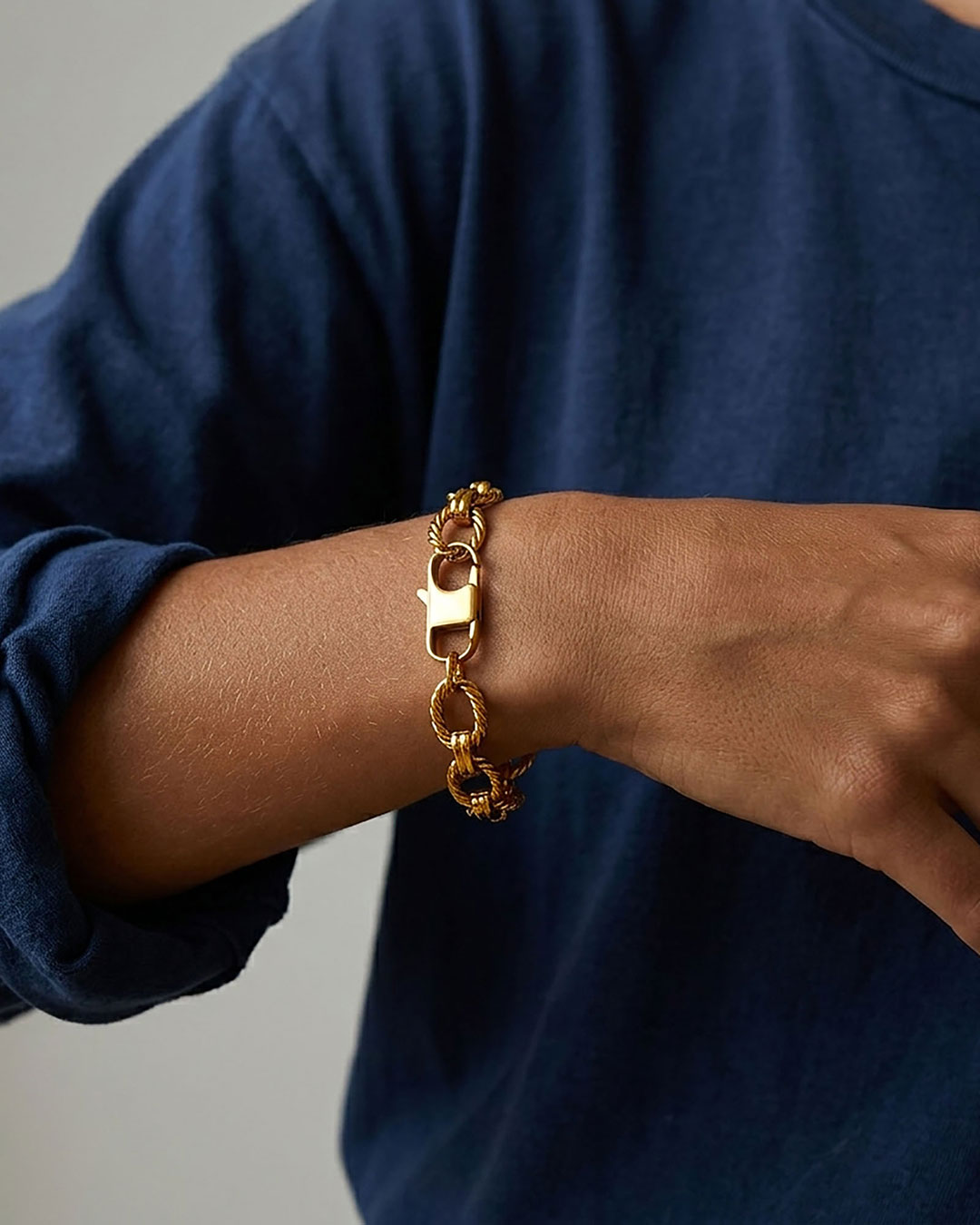 A stainless steel gold chain bracelet with twisted oval links on a woman's wrist.