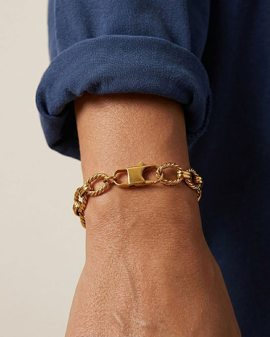 A stainless steel gold chain bracelet with twisted oval links on a woman's wrist.