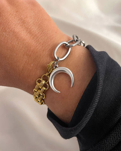 Gold and silver bracelet with a crescent moon charm on a wrist against a neutral background
