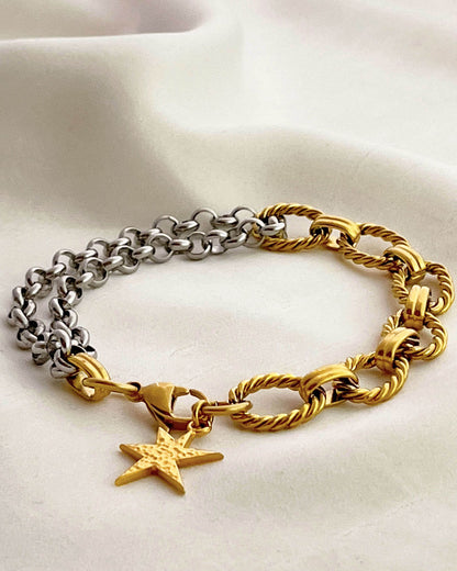 Two chain bracelets, one gold and one silver with a gold charm charm on a light background