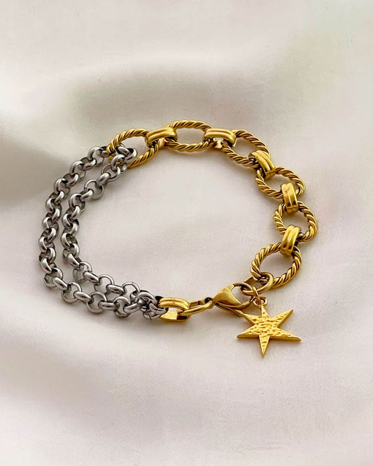 Two chain bracelets, one gold and one silver with a gold charm charm on a light background